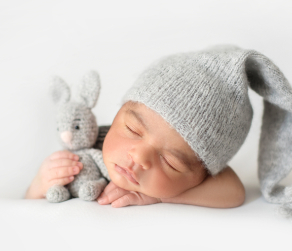 cute-infant-sleeping-with-grey-crocheted-hat-with-toy-rabbit 1